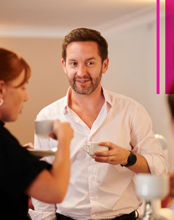 A member of our team is shown talking to a colleague. Both of them are drinking coffee. 